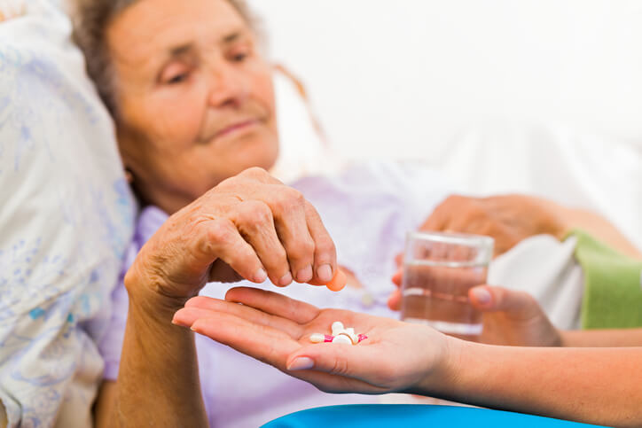 A health care assistant training grad administering medication to an elderly bedridden client.