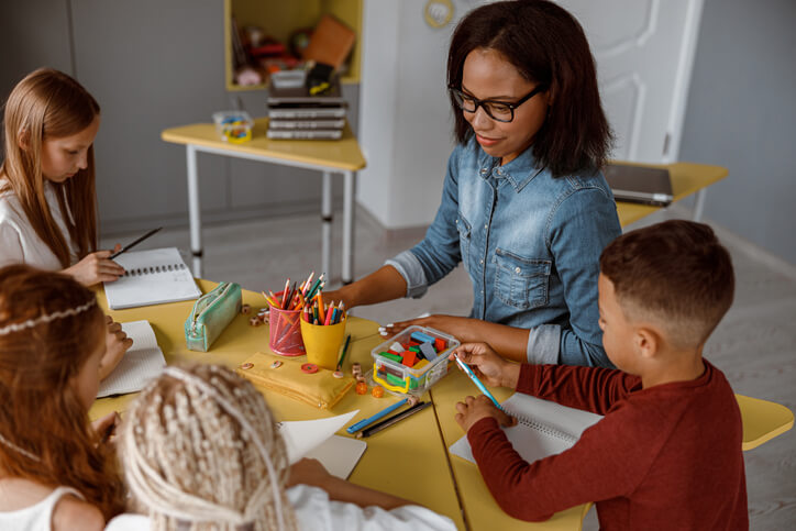 An education assistant training grad helping a group of students with a craft activity