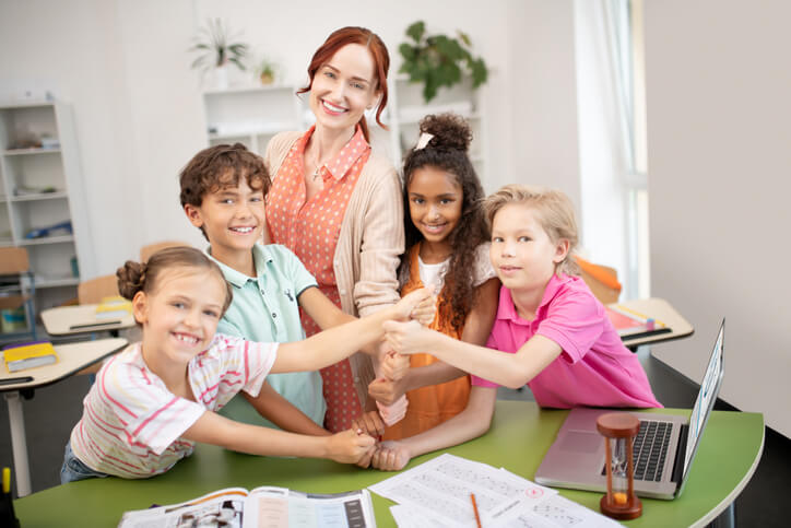 An education assistant training grad posing with a group of happy students