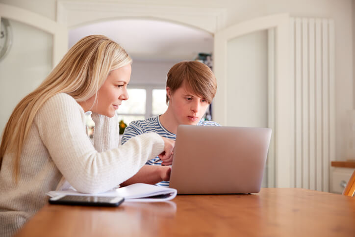 A female education assistant teaching a special needs child how to use the laptop after completing her education assistant training