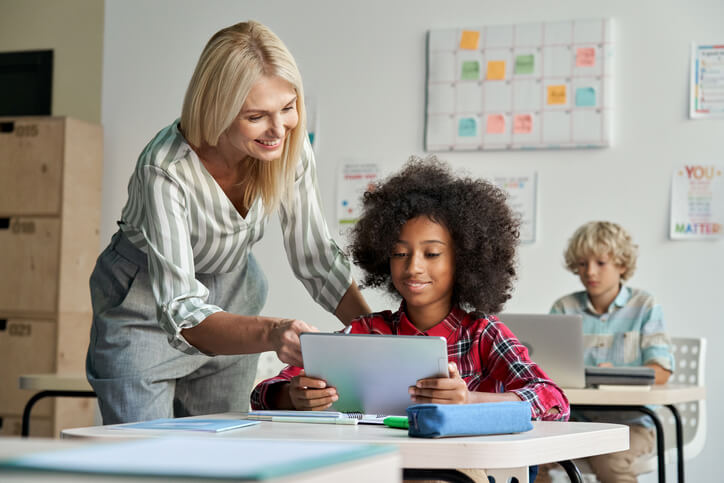 A smiling female education assistant assisting a female pupil in a classroom