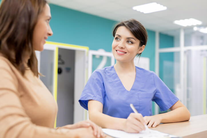 A cheerful female medical office assistant interacting with a patient after completing her medical office assistant training