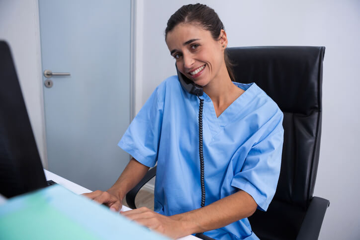 A medical office management training grad using the phone and writing notes