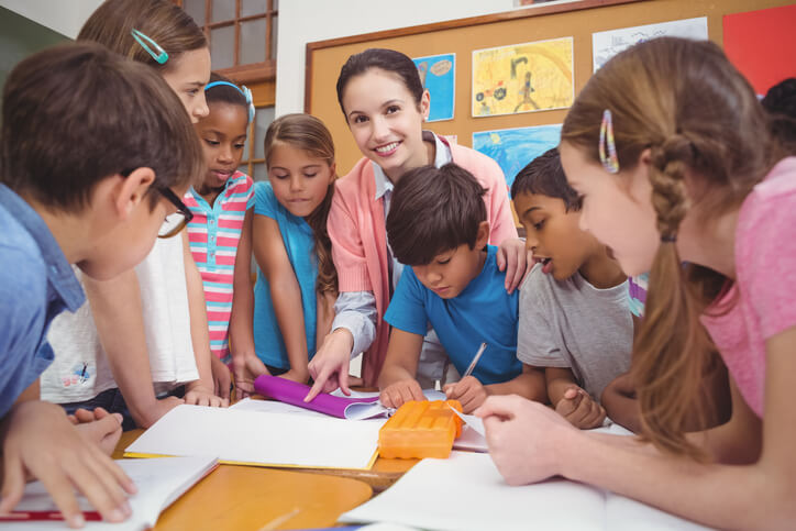 A happy female education assistant working together with pupils in a classroom after completing her education assistant training