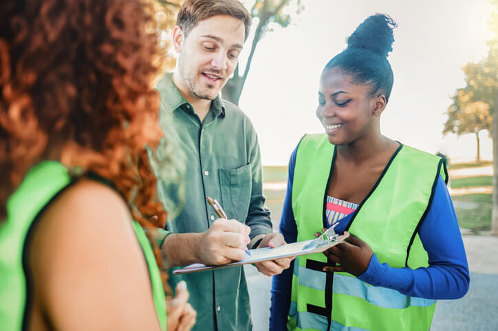 A smiling community support worker helping a pair of volunteers with documentation.
