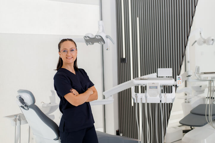 A dental assistant posing in a clinic next to dental equipment