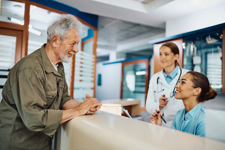 A medical office management training grad helping an elderly patient at the front desk