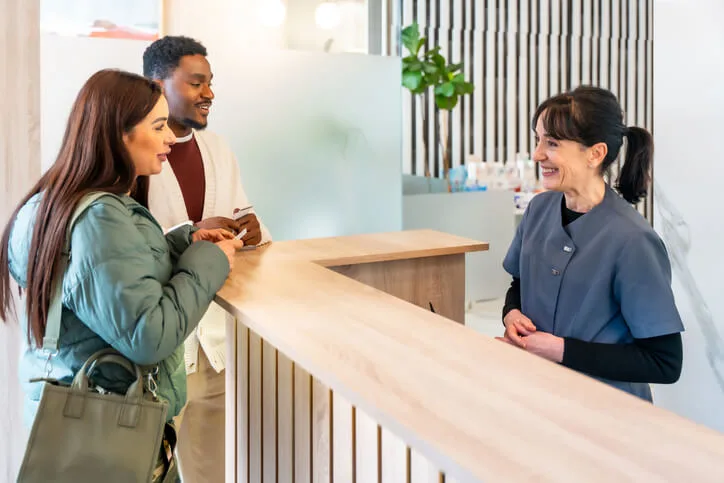A dental receptionist communicates with patients at a busy dental reception desk