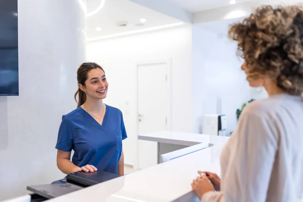 Medical and dental office administration student welcoming patients at a clinic reception desk.